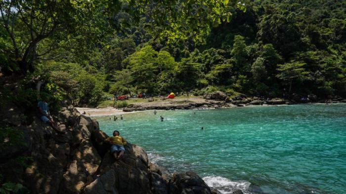 المناظر الطبيعية في الشاطئ المحاط بتلال خضراء تُضفي على المكان أجواء هادئة ومنعشة