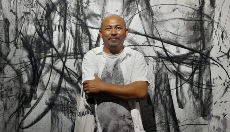 الفنان التشكيلي إيوان يوسف يقف أمام أحد أعماله في معرض 